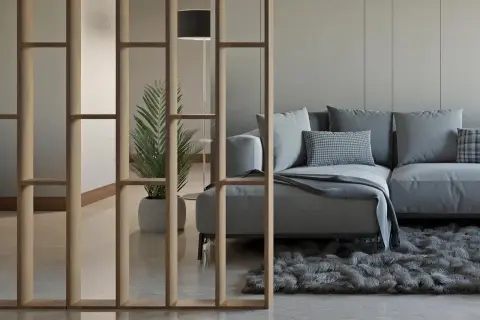 Ein modernes Wohnzimmer mit einer stilvollen Trennwand, die man auch selber bauen könnte. Ein bequemes Sofa und eine Pflanze schaffen Gemütlichkeit.