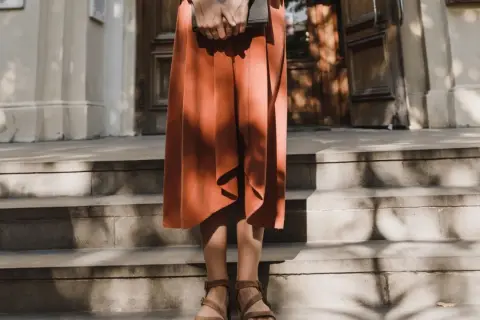 Kobieta w pomarańczowej sukience i sandałach trzyma książkę. Stylizacja idealna do letniego lookbooka.