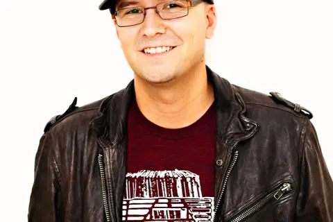 A smiling man in a leather jacket and cap, possibly inspired by the creative spirit behind Luke Laird songs.