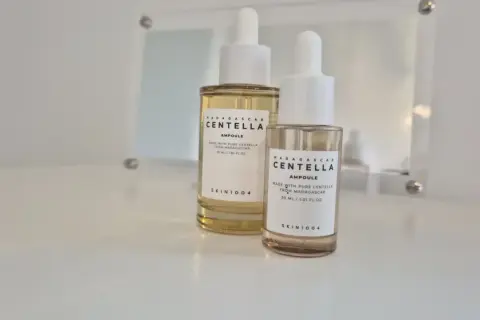 Dwie buteleczki z pipetką zawierające **centella ampoule** od SKIN1004, jedna większa, druga mniejsza, stoją na białej powierzchni.