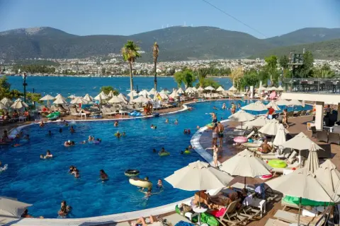 Wakacje all inclusive Polska: ludzie kąpią się w basenie, opalają na leżakach pod parasolami, w tle morze i góry.
