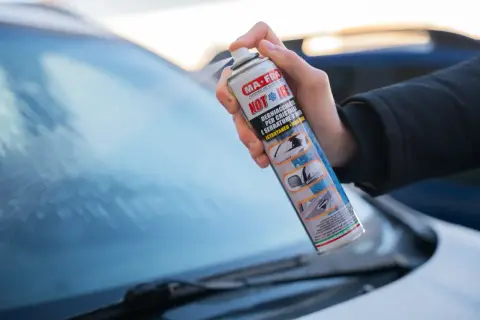 Mano che spruzza un prodotto per togliere il ghiaccio dal parabrezza dell'auto.