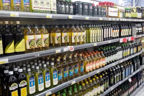 Scaffali di un supermercato pieni di bottiglie di olio d'oliva. Quante olive per un litro di olio? La risposta è nella varietà di marche e formati.