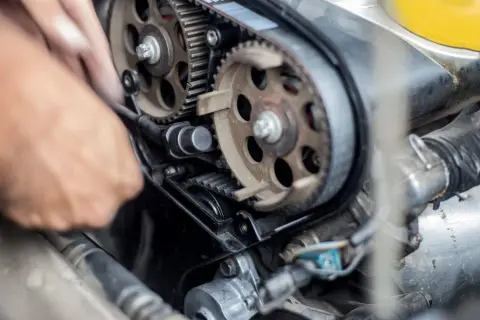 Mano che lavora per cambiare cinghia distribuzione motore auto, con ingranaggi e pulegge in primo piano.