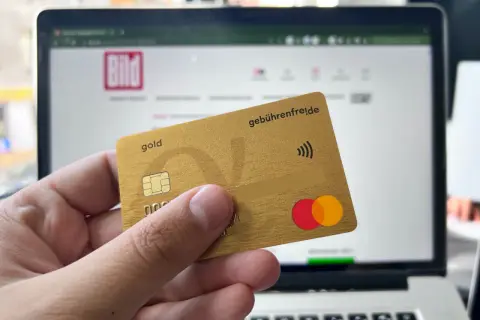 Goldene Kreditkarte mit "gebührenfrei.de" und Mastercard-Logo vor einem Laptop mit BILD-Logo. Erste Erfahrungen mit der Advanzia Bank.