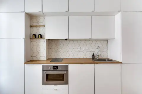 Moderna cucina bianca con paraschizzi a esagoni geometrici, piano in legno e forno in acciaio.