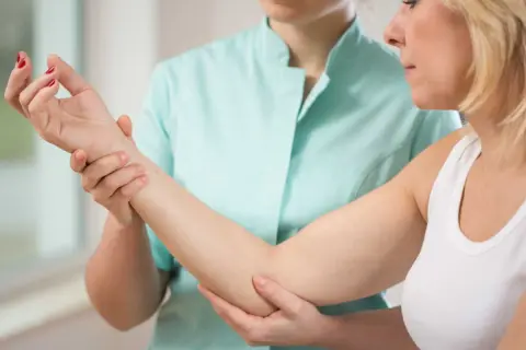 Une thérapeute examine le bras d'une patiente, possiblement pour une nevralgie cervico brachiale.