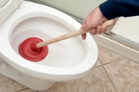 Main tenant utilise une ventouse pour tenter, en vain, de déboucher les toilettes.