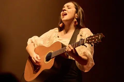 Valeria Castro Zaragoza canta con pasión, guitarra en mano, bajo una luz cálida.