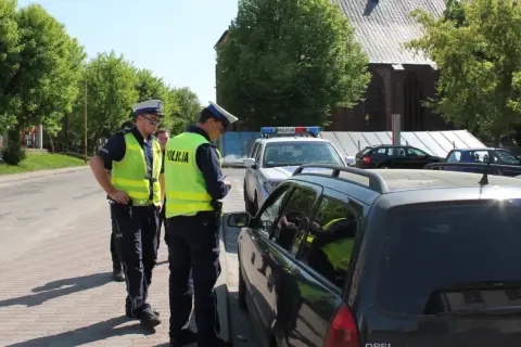 Policjanci wypisują mandat za jazdę po chodniku. Jeden z funkcjonariuszy spisuje dane kierowcy w samochodzie.