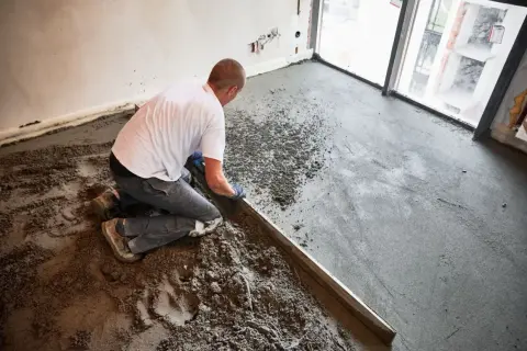 Budowlaniec wyrównuje wylewkę z **anhydrytu** za pomocą łaty.