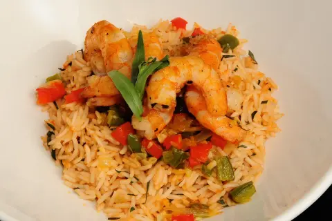 Delicioso arroz con gambas y verduras, con pimientos rojos y verdes, y una hoja verde decorativa.