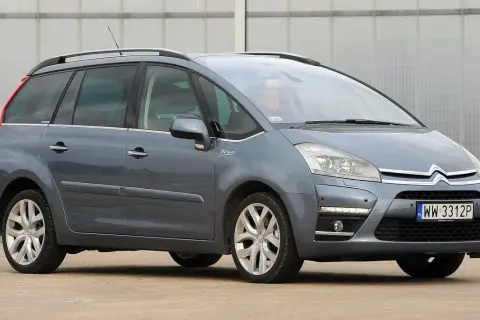 Szary Citroen C4 Grand Picasso 2.0 HDI z kierowcą za kierownicą, zaparkowany przed budynkiem.