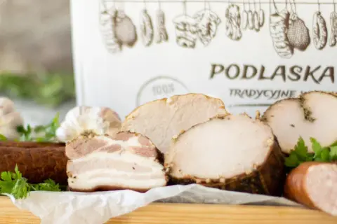 Swojskie wyroby wędliniarskie z Podlaskiej Chaty: kiełbasa, boczek, pieczone mięsa i czosnek. Tradycyjne smaki.