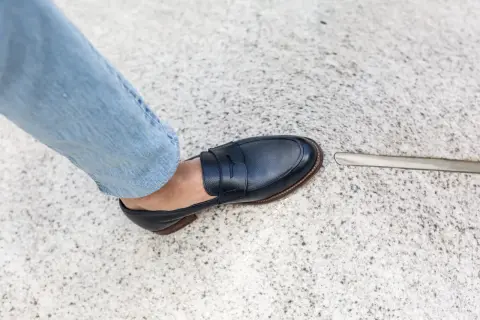 Un homme en jean bleu porte une chaussure de ville marine. L'outil à côté suggère une envie de ressemeler chaussures.