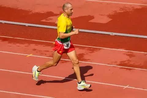 Un athlète en tenue jaune et rouge court sur une piste mouillée, visant le record du monde de vitesse à pied.