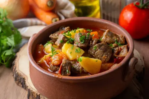 Gulasz węgierski w glinianej misce z ziemniakami, mięsem i warzywami, ozdobiony natką pietruszki.