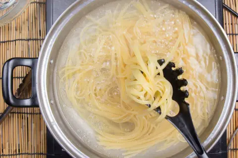 Spaghetti kochen in sprudelndem Wasser. Ein schwarzer Pastalöffel hebt eine Portion heraus, um zu zeigen, wie kleben spaghetti nach dem kochen nicht zusammen.