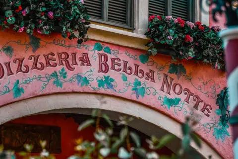 Różowa fasada Pizzerii Bella Notte ozdobiona winoroślą i kwiatami.