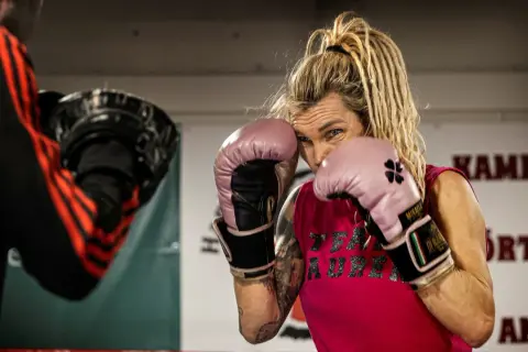 Mikaela boxare i rosa handskar, redo för träning. Hennes blick är fokuserad, med dreadlocks som ramar in ansiktet.