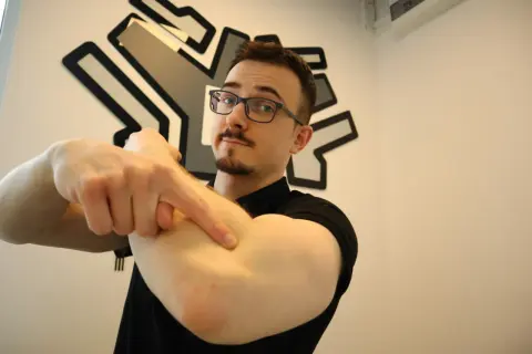 Mężczyzna w okularach wskazuje palcem na zewnętrzną stronę łokcia.