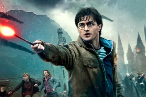 Harry Potter z różdżką w dłoni, w tle bitwa o Hogwart. To scena z serii filmowej Harry Potter.