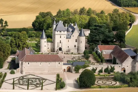 Vue aérienne du **château du Riveau**, un édifice médiéval entouré de jardins à la française et de champs dorés.