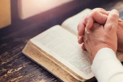 Dłonie złożone nad otwartą księgą, której strony zawierają tekst apostolski.