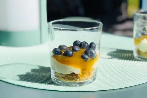 En läcker cheesecake i glas med blåbär och en gyllene sås. Perfekt för en solig sommardag.