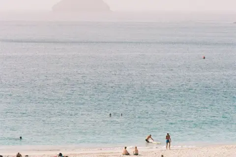 Ludzie odpoczywają na plaży, w tle widać ocean i wyspy. Zastanawiasz się, ile trwa lot na Wyspy Zielonego Przylądka?