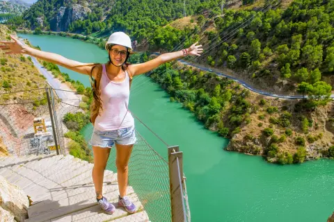 Glad kvinna med armarna utsträckta njuter av en fantastisk caminito del rey vandring med turkos flod nedanför.