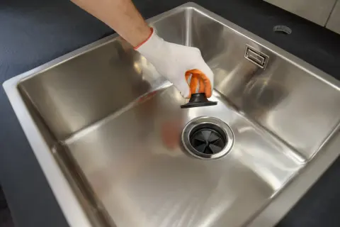 Ręka w rękawiczce wkłada czarny korek przelewowy do umywalki.