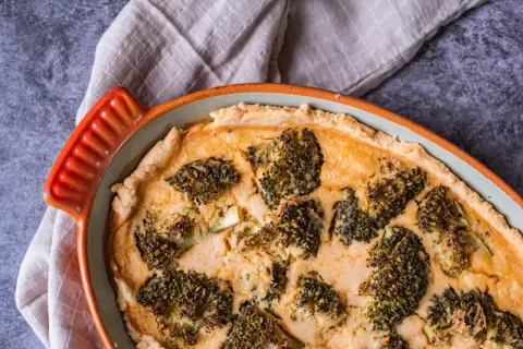 En gyllene ost och broccolipaj i en orange kantig form, redo att serveras.