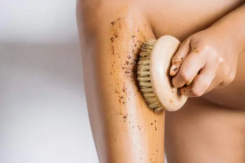 Mano che applica fango dimagrante con spazzola su gamba. Esfoliazione e benessere per la pelle.