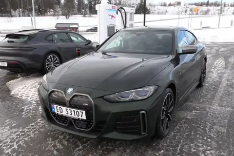 Zielone BMW i4 na ładowarce w zimowy dzień. Obok stoi ciemny Porsche Taycan.