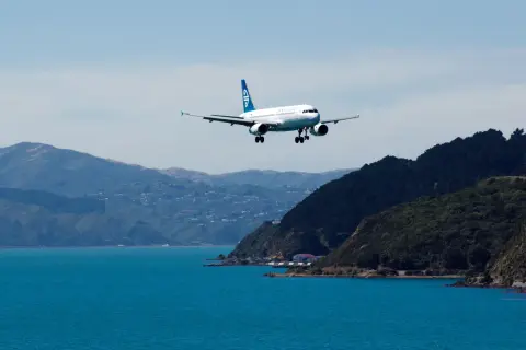 Samolot Air New Zealand ląduje nad turkusową wodą, zbliżając się do wybrzeża. Zastanawiasz się, ile kosztuje lot do Nowej Zelandii?