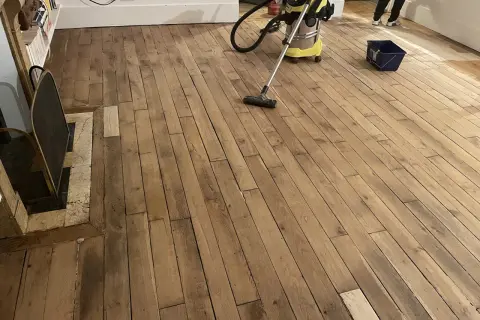 Un aspirateur nettoie un parquet en bois vitrifié, prêt pour une nouvelle couche de protection.