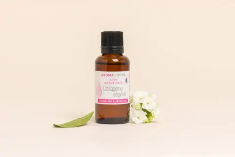 Flacon de collagène végétal Aroma-Zone, aux bienfaits hydratants et repulpants, entouré de fleurs blanches et d'une feuille verte.