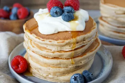 Fluffige Bananenpfannkuchen mit Sahne, Beeren und Honig. Ein köstlicher Frühstückstraum!