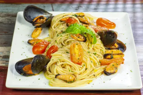 Un piatto invitante di spaghetti con le cozze e pomodorini, guarnito con basilico fresco.