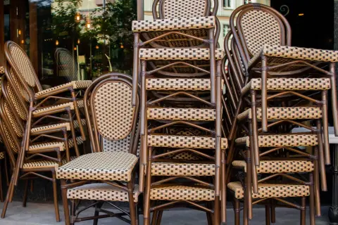 Gestapelte braune Bistrostühle mit geflochtenen Sitzflächen und Rückenlehnen vor einem Restaurant.