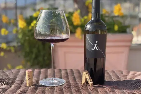 Un calice di vino rosso e una bottiglia di Negroamaro Puglia, con tappo e cavatappi, su un tavolo all'aperto.