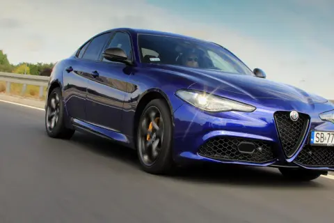 Błękitne Alfa Romeo Giulia Veloce pędzi po drodze, błyszcząc w słońcu.