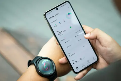 Ręka trzyma telefon Samsung z aplikacją Samsung Health, pokazującą kroki i aktywność. Zegarek na nadgarstku synchronizuje dane, pomagając jak znaleźć telefon Samsung.