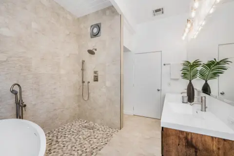 Une salle de bain moderne avec une baignoire îlot, une douche à l'italienne aux galets et un double lavabo. Un exemple de les plus belles douches à l'italienne.