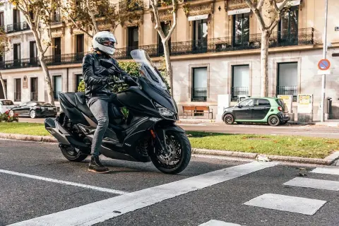 Conductor con casco blanco en un scooter negro, listo para rodar. Una imagen que evoca las mejores marcas de motos y la libertad en la ciudad.
