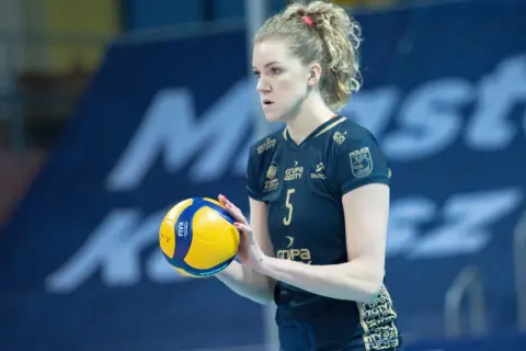 Agnieszka Korneluk, siatkarka z numerem 5, trzyma piłkę. Jej mąż pewnie kibicuje jej z trybun.