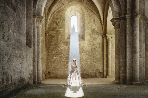 Cristina Vatielli, vestita di bianco, in piedi sotto un raggio di luce in un'antica abbazia.