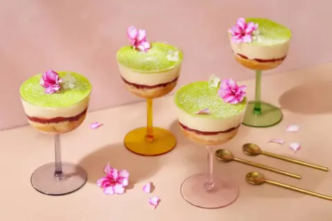 Fyra vackra prinsesstårtor i glas, dekorerade med blommor och strösocker. Perfekt för en festlig fika.