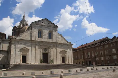 Il Duomo di Torino, con la sua imponente facciata in pietra e la cupola maestosa, si staglia sotto un cielo azzurro punteggiato di nuvole bianche.